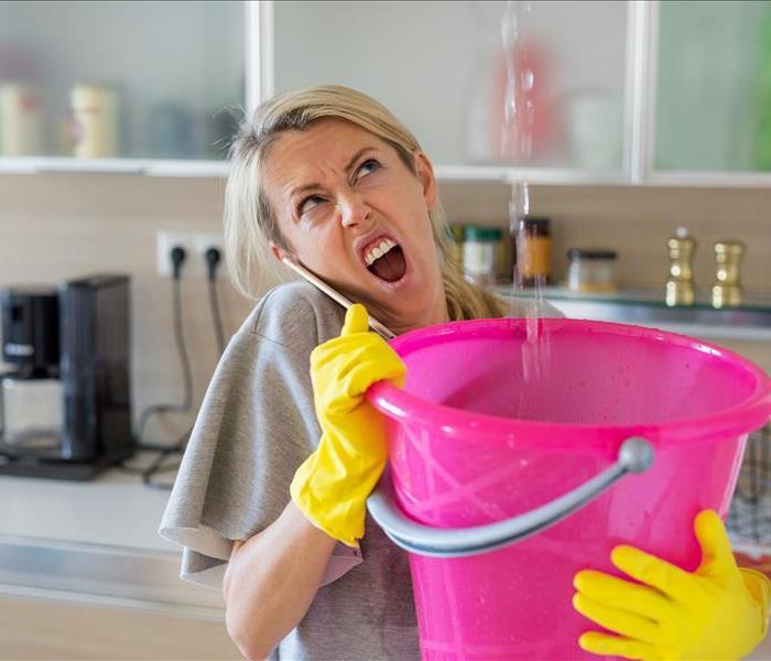 woman holding bucket over ceiling water leak